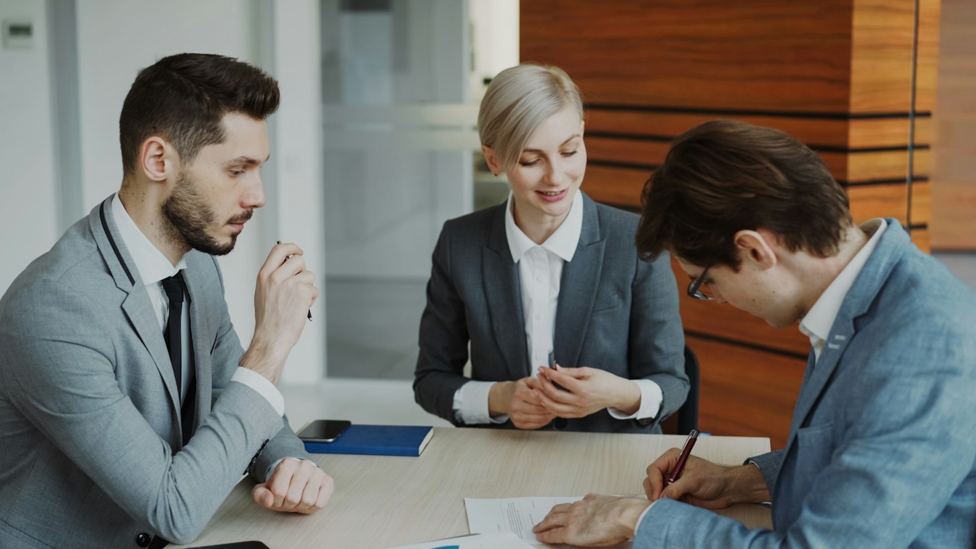 A client signing documents in a meeting with two advisers